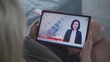 © Framestock - Tablet screen shows TV news broadcast with female newscaster. Caucasian woman watching breaking news about United States presidential elections using digital tablet while lying on sofa. Close Up.
