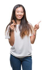 Sticker - Young asian woman eating chocolate energetic bar over isolated background very happy pointing with hand and finger to the side