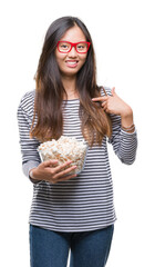 Wall Mural - Young asian woman eating popcorn over isolated background with surprise face pointing finger to himself