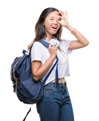 Canvas Print - Young asian woman wearing backpack and headphones over isolated background with happy face smiling doing ok sign with hand on eye looking through fingers