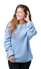 Poster - Young beautiful brunette woman wearing blue winter sweater over isolated background smiling with hand over ear listening an hearing to rumor or gossip. Deafness concept.