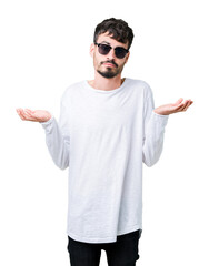 Poster - Young handsome man wearing sunglasses over isolated background clueless and confused expression with arms and hands raised. Doubt concept.