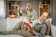 © Miljan Živković - Senior husband lying down on sofa and read book whit his mature wife