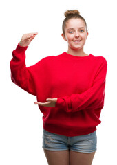 Poster - Young blonde woman wearing bun and red sweater gesturing with hands showing big and large size sign, measure symbol. Smiling looking at the camera. Measuring concept.