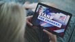 © Framestock - Close up of Caucasian woman watching political advertising or video content about the United States presidential elections using tablet computer while lying on sofa at home. Election Day in USA.