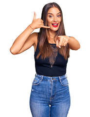 Canvas Print - Young hispanic woman wearing casual clothes smiling doing talking on the telephone gesture and pointing to you. call me.