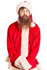 Sticker - Handsome young red head man with long beard wearing santa claus costume puffing cheeks with funny face. mouth inflated with air, crazy expression.