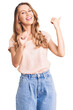 © Krakenimages.com - Young beautiful caucasian woman with blond hair wearing casual clothes pointing to the back behind with hand and thumbs up, smiling confident