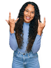 Young hispanic woman with curly hair wearing casual clothes shouting with crazy expression doing rock symbol with hands up. music star. heavy concept.