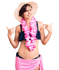 Wall Mural - Beautiful young woman with short hair wearing bikini and hawaiian lei looking confident with smile on face, pointing oneself with fingers proud and happy.