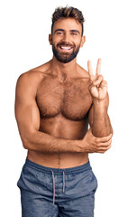 Wall Mural - Young hispanic man wearing swimwear shirtless smiling with happy face winking at the camera doing victory sign. number two.