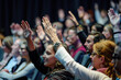 © Mnur - A group of people are in a room, all raising their hands in unison
