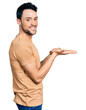© Krakenimages.com - Hispanic man with beard wearing casual t shirt pointing aside with hands open palms showing copy space, presenting advertisement smiling excited happy