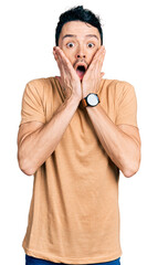 Poster - Hispanic man with beard wearing casual t shirt afraid and shocked, surprise and amazed expression with hands on face