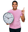© Krakenimages.com - Young handsome hispanic man holding big clock surprised with an idea or question pointing finger with happy face, number one