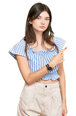 Poster - Young beautiful caucasian girl wearing casual clothes pointing with hand finger to the side showing advertisement, serious and calm face