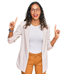 Young african american girl wearing business clothes smiling amazed and surprised and pointing up with fingers and raised arms.