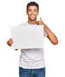 © Krakenimages.com - Young handsome african american man holding blank empty banner smiling happy and positive, thumb up doing excellent and approval sign