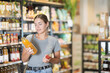 © JackF - Young woman in bio supermarket buys drink. Girl buyer examines packaging bottle of product and reads information on label