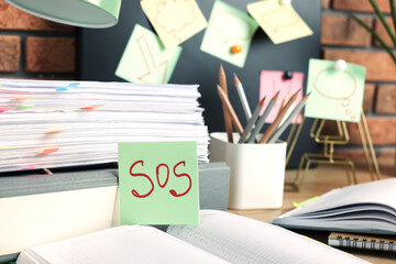 Sticky note with word SOS and stationery on table at workplace