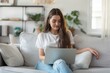 © InfiniteStudio - Young woman using laptop on cozy couch, home office concept