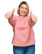 © Krakenimages.com - Hispanic woman with pink hair wearing casual winter sweater approving doing positive gesture with hand, thumbs up smiling and happy for success. winner gesture.