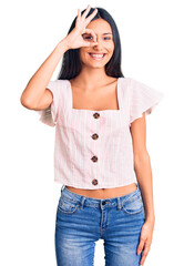 Poster - Young beautiful latin girl wearing casual clothes smiling happy doing ok sign with hand on eye looking through fingers