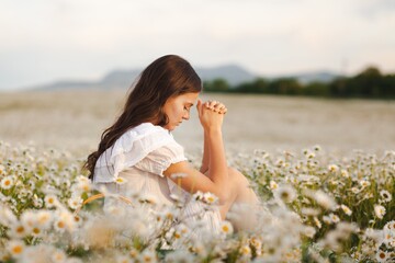 Poster - Woman praying on nature chamomile field background.