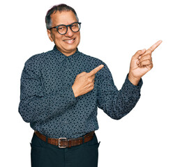 Poster - Middle age indian man wearing casual clothes and glasses smiling and looking at the camera pointing with two hands and fingers to the side.