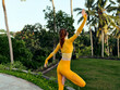 © SHOTPRIME STUDIO - Serene woman in yellow yoga attire strikes a pose amidst lush palm trees in a tropical paradise