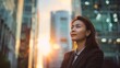 © Sirichat. Camphol - Happy successful and wealthy Asian businesswoman standing in big city on modern skyscraper road at sunset thinking about successful vision
