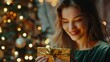© Creations Photo  - Gorgeous young beautiful woman opening a golden gift box, light shines on her beautiful face. Attractive smiling model wears a velvet emerald dress, looks happy. Christmas tree lights on background
