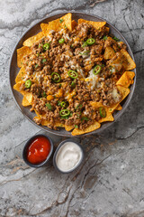 Wall Mural - Loaded Beef and Cheese Nachos with jalapeno peppers and sauces closeup on the plate on the table. Vertical top view from above