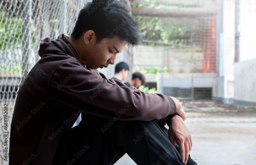 Asian preteen boy in a black hoodie sits with his knees pressed against ...
