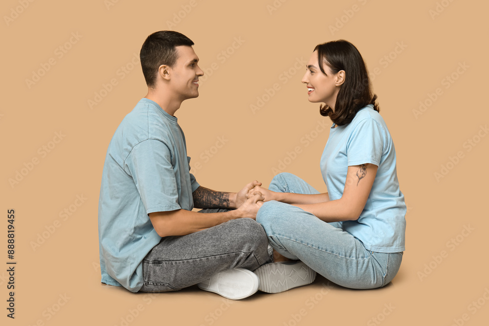 Happy young couple sitting on floor and holding hands on beige background