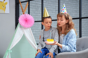 Poster - Mother and her cute little boy blowing out candle on birthday cake in decorated room