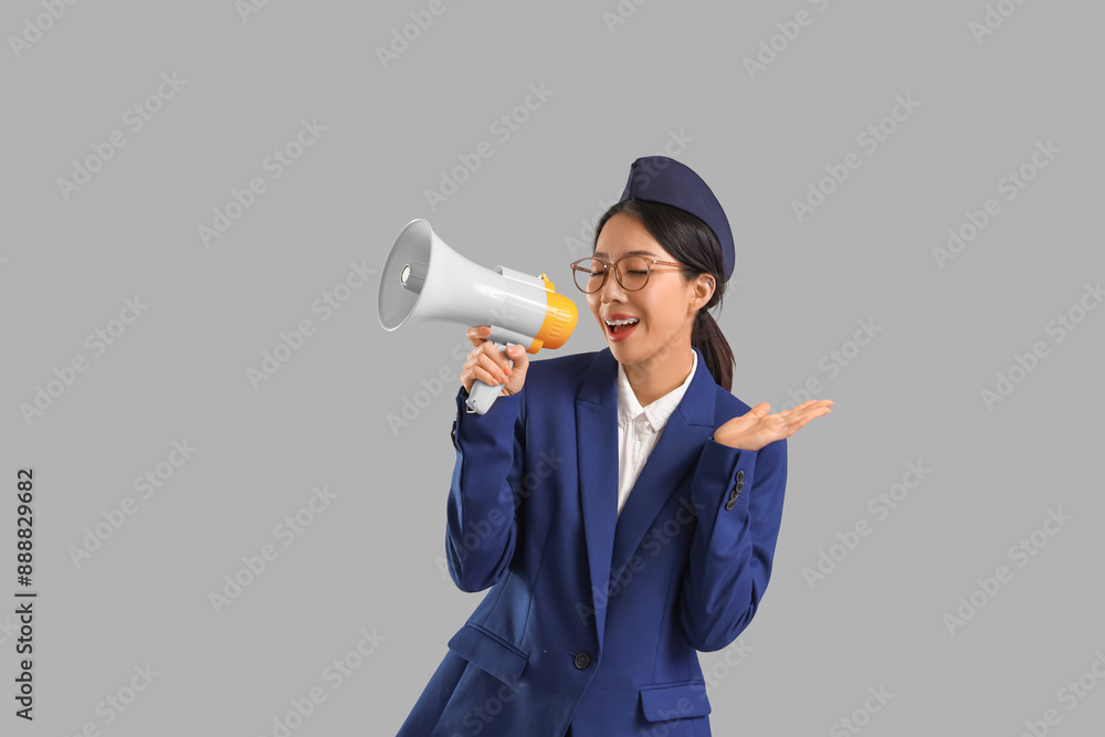 Young Asian stewardess with megaphone on grey background