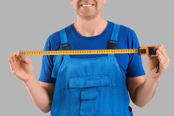 Canvas Print - Male construction worker with measuring tape on grey background, closeup