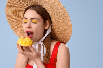 Poster - Beautiful young woman with cut sweet mango fruit on blue background