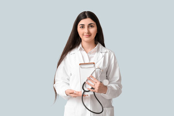 Beautiful young female doctor with clipboard and stethoscope on white background