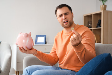 Wall Mural - Bankrupt young man with piggy bank and coin at home