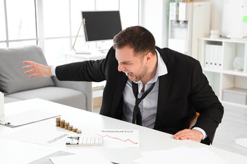 Wall Mural - Angry bankrupt businessman with stacks of coins on table in office