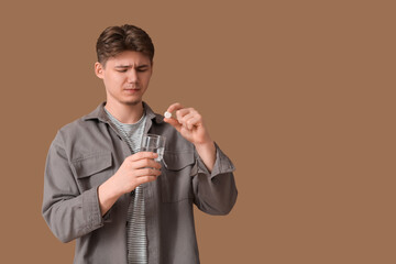 Poster - Young man putting soluble tablet for headache into glass of water on brown background