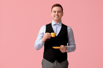 Young man holding cup of fresh coffee and saucer on pink background