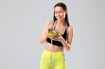 Poster - Beautiful young happy woman with measuring tape and bowl of fresh salad on grey background. Weight loss concept