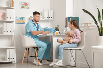 Poster - Male pediatrician talking to little girl at table in clinic