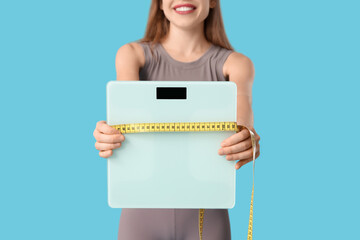 Poster - Sporty young woman with measuring tape and scales on blue background. Diet concept