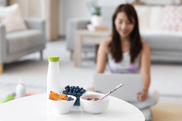 Wall Mural - Sporty young Asian woman with laptop at home, focus on tasty yogurt and fruits on table