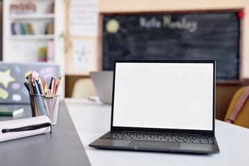 Background shot of laptop empty mockup screen on table in front of camera in primary school classroom, copy space