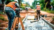 © Rossarin - Construction worker using a surveying tool on a construction site.  Two other workers are visible in the background.